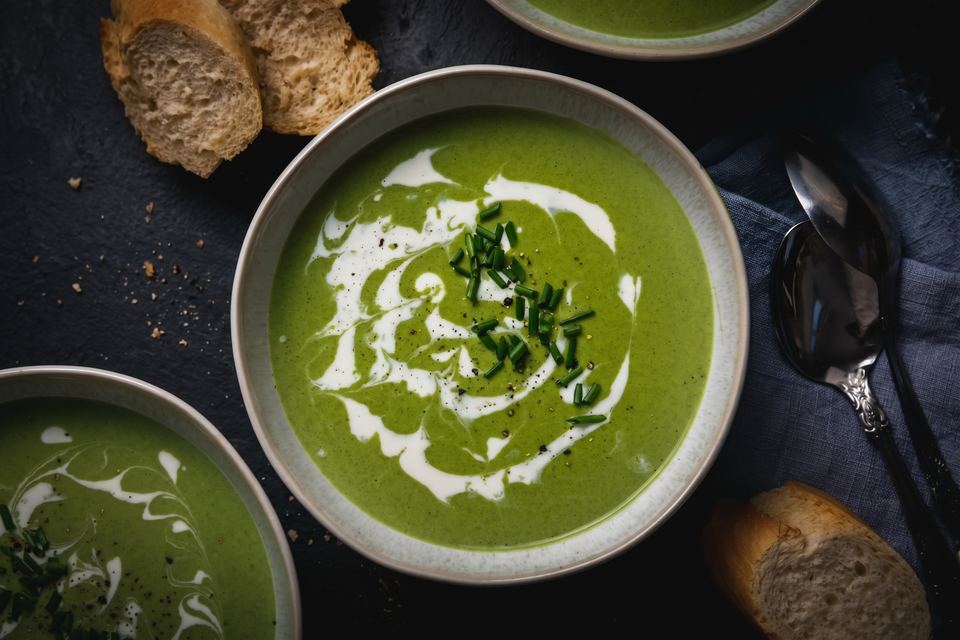 Bowl of bright green spinach soup finished with cream and chives, served with bread
